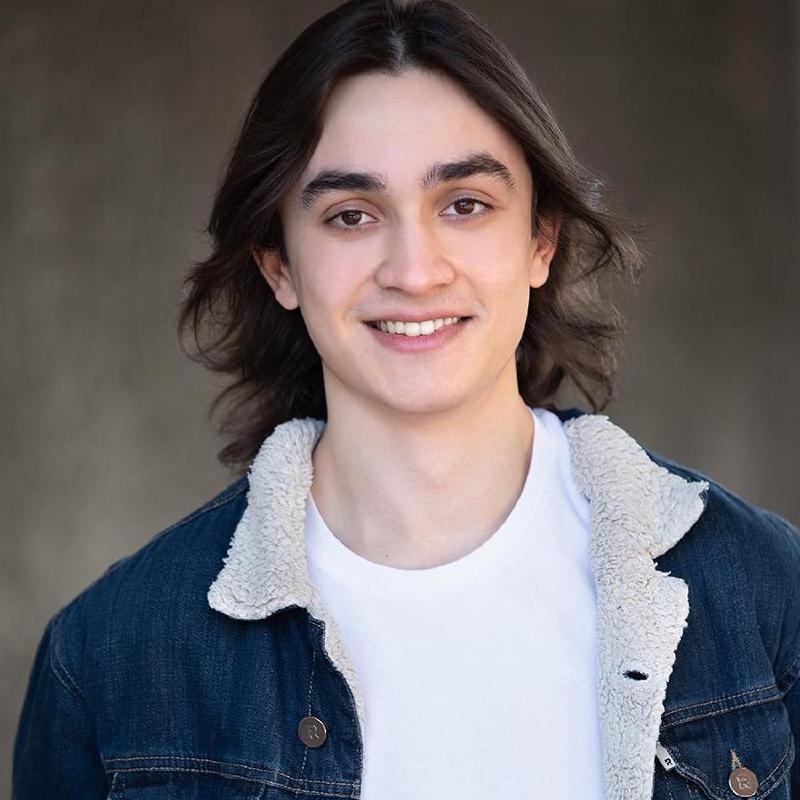 A headshot of myself. I am a young man with brown long hair. I am wearing a white shirt with a blue jean jacket, smiling at the camera.